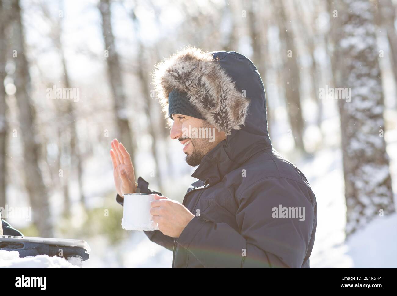 Homme souriant entrepreneur gestant sur appel vidéo tout en prenant le café en hiver Banque D'Images