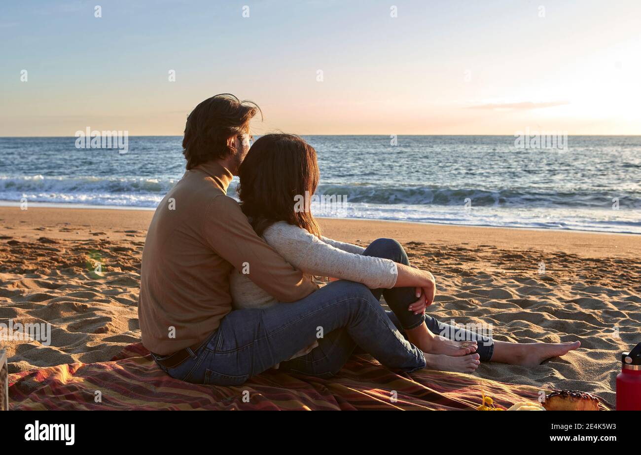 Jeune couple regardant la vue sur la mer tout en étant assis sur la plage Banque D'Images
