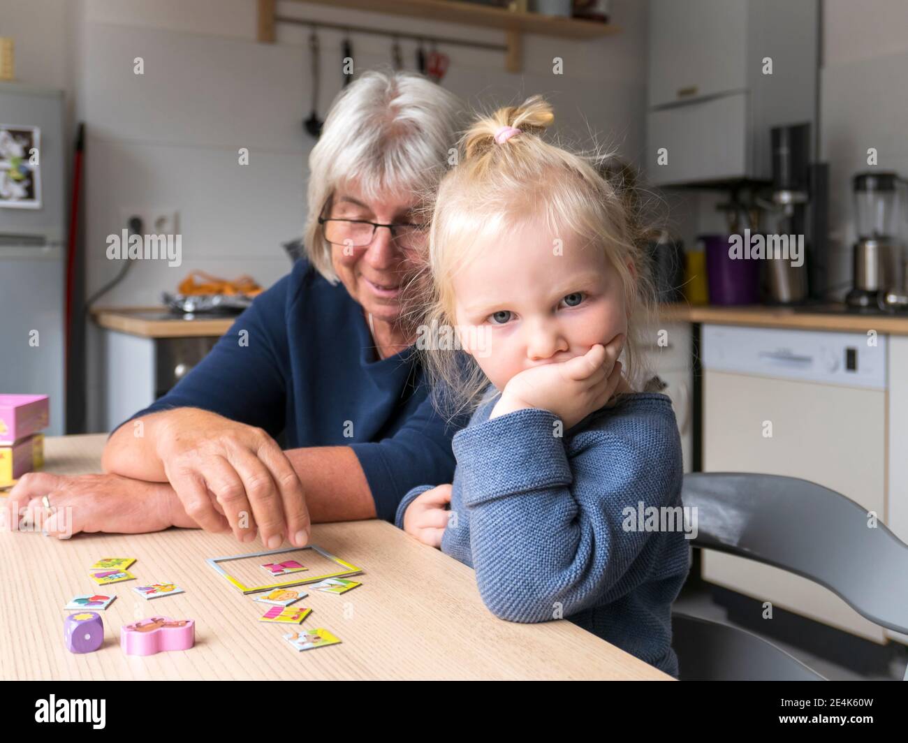 Une fille blonde bouleversée assise par une grand-mère jouant au puzzle au restaurant table dans la cuisine Banque D'Images