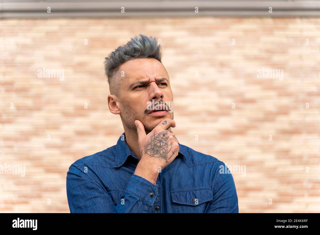 Homme tatoué et attentionné avec la main sur le menton en regardant loin contre mur Banque D'Images