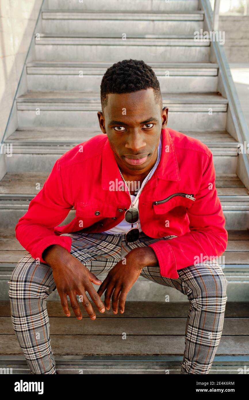 Portrait d un jeune homme en veste rouge et pantalon a carreaux assis sur des marches a l exterieur Photo Stock Alamy