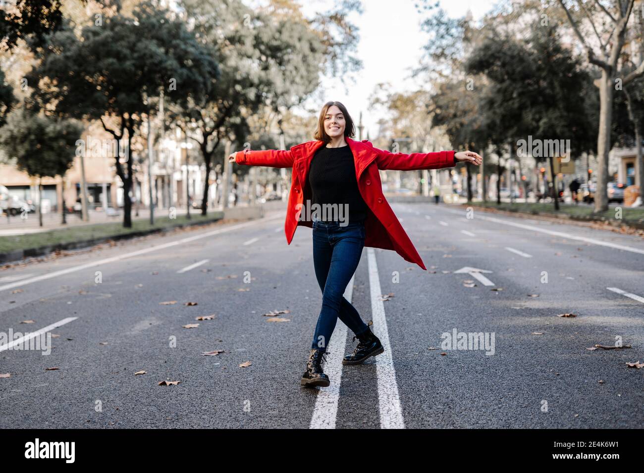 Jeune femme souriante faisant du ballet avec les bras étirés sur la route Banque D'Images