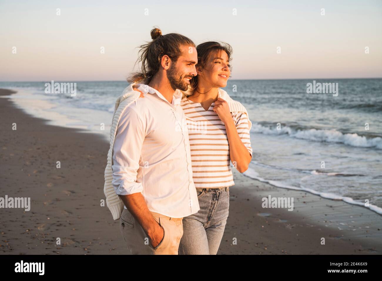 Jeune couple souriant qui regarde loin en marchant à la plage pendant vacances Banque D'Images