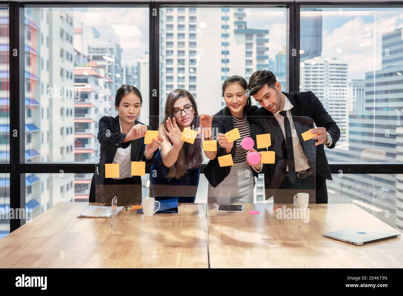 Équipe commerciale multiethnique en brainstorming avec des notes adhésives de couleur pastel sur le tableau dans un bureau moderne du quartier des affaires Banque D'Images