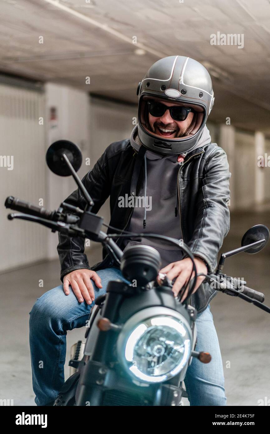 Homme joyeux portant un casque et des lunettes de soleil assis sur une moto  dans le parking Photo Stock - Alamy