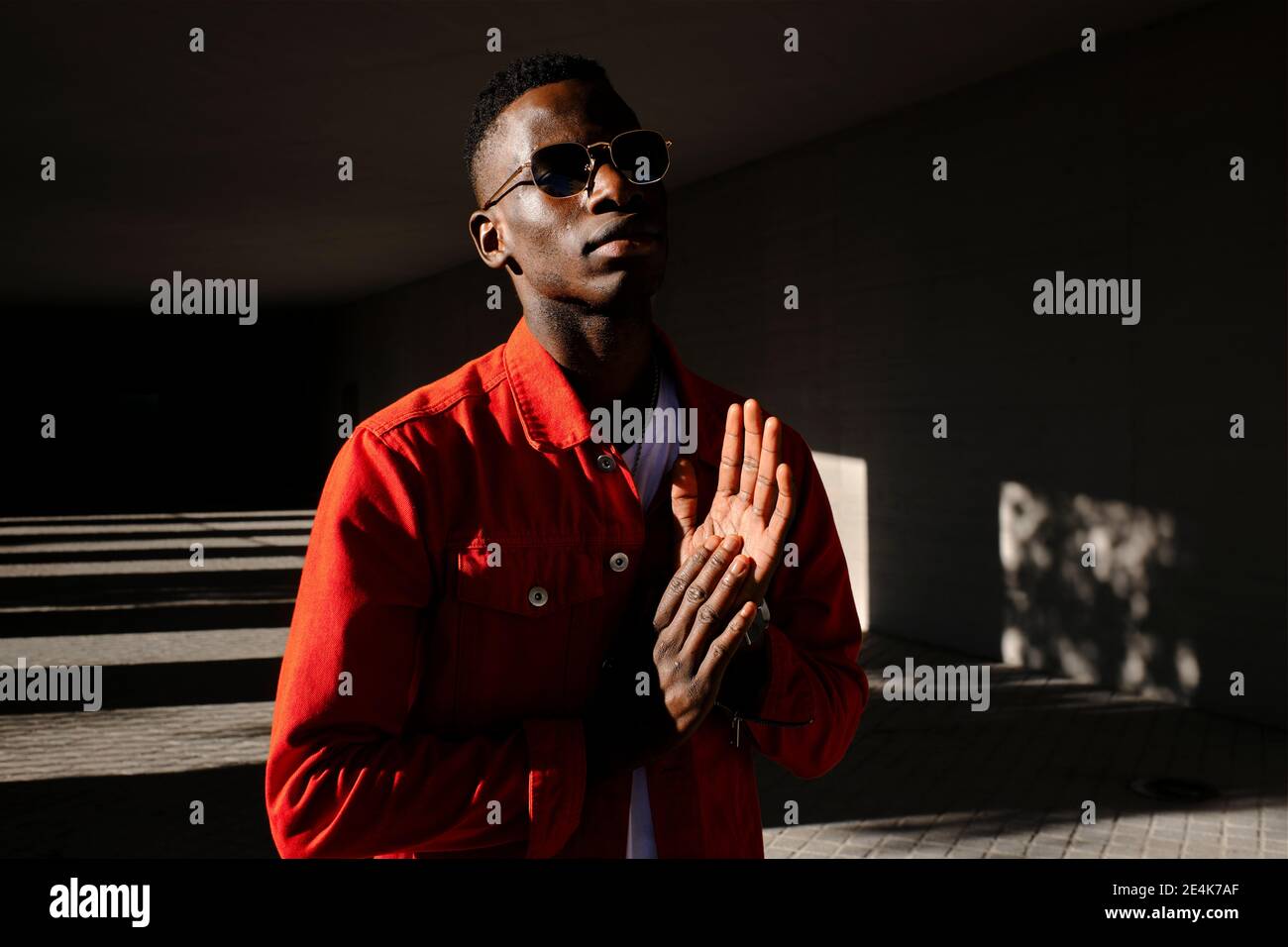 Jeune homme en veste rouge et lunettes de soleil à l'extérieur Banque D'Images