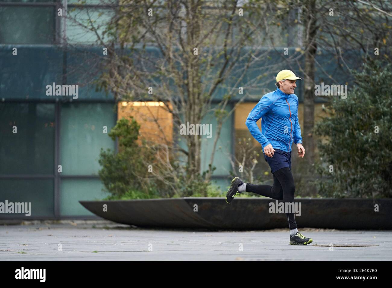 Homme mûr souriant qui court sur le sentier contre le bâtiment résidentiel Banque D'Images