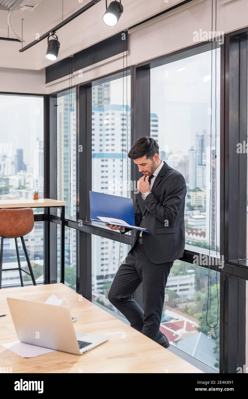 Un homme d'affaires caucasien intelligent qui se tient avec l'analyse de documents financiers dans moderne bureau dans le quartier des affaires Banque D'Images