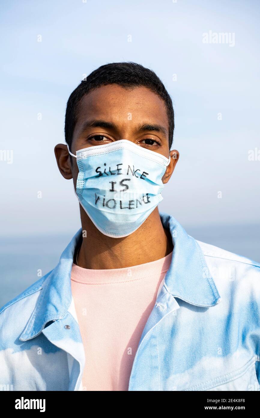 Jeune homme portant un masque écrit « Silence is violence » debout à l'extérieur Banque D'Images