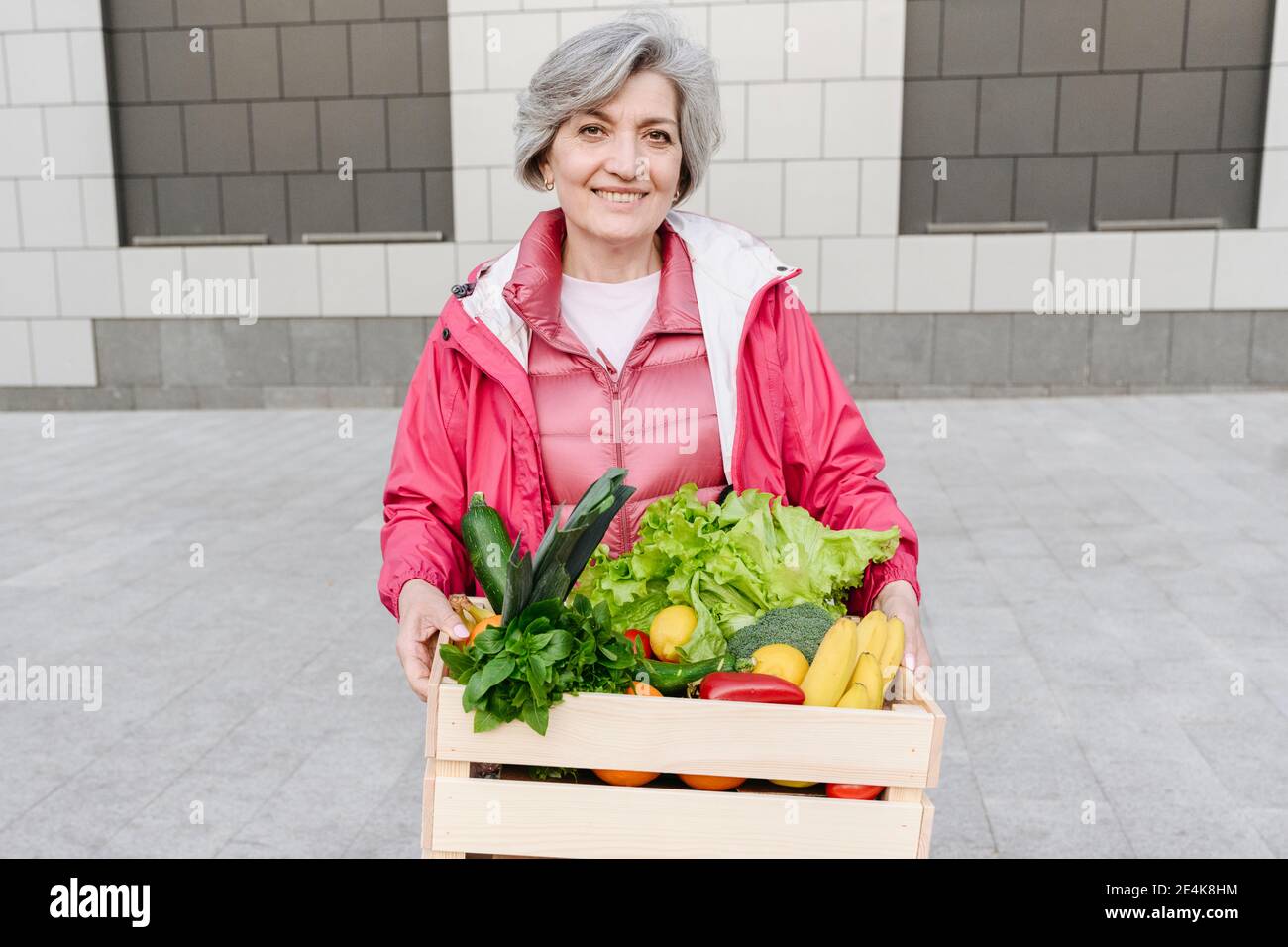 Femme mûre souriante avec des légumes et de la caisse de nourriture contre le mur Banque D'Images