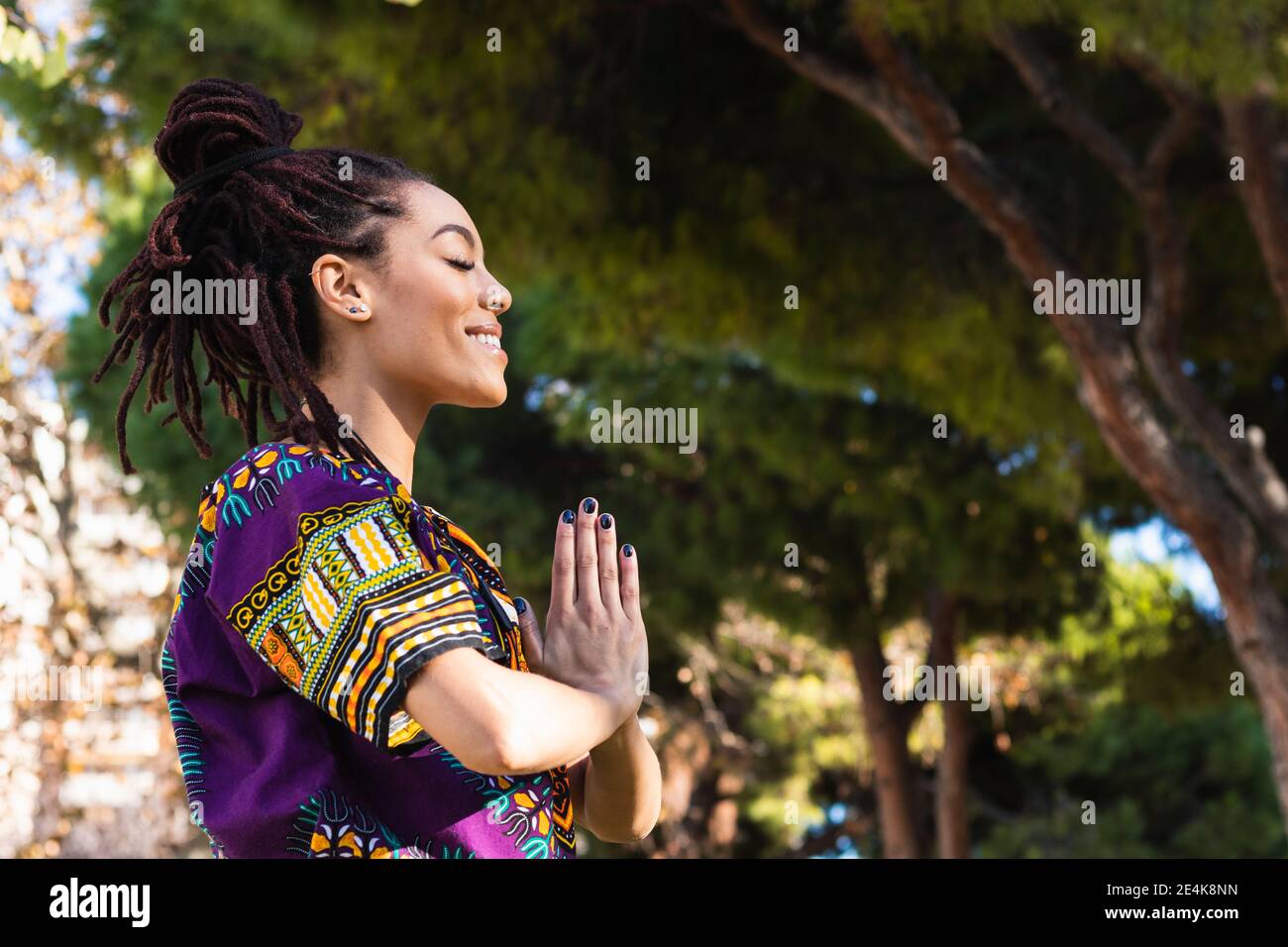 Souriante belle jeune femme méditant avec les mains jointes en pratiquant yoga au parc Banque D'Images