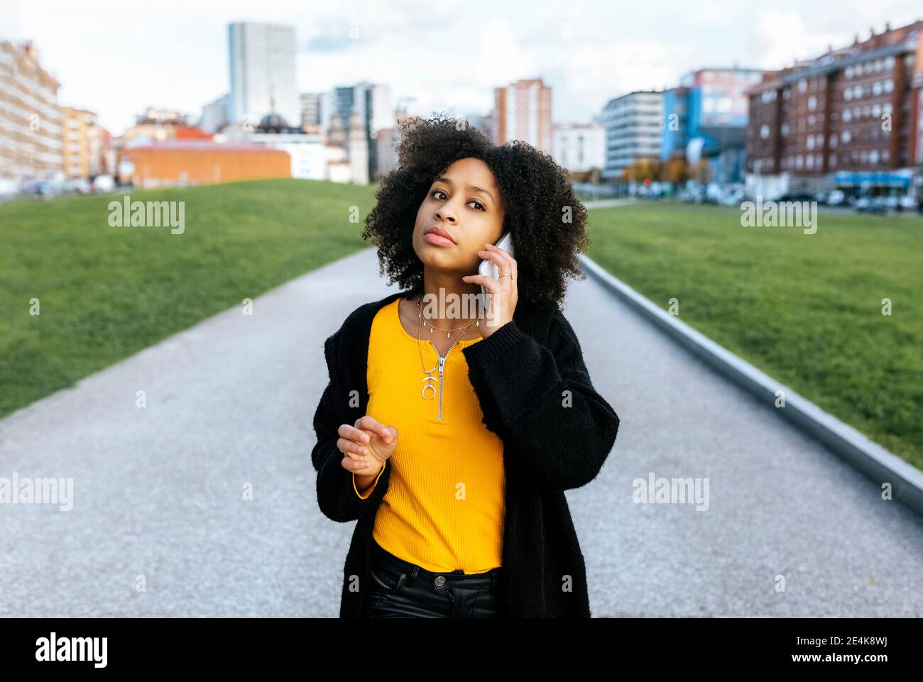 Jeune femme avec des cheveux afro parlant sur le smartphone pendant debout sur le sentier de la ville Banque D'Images