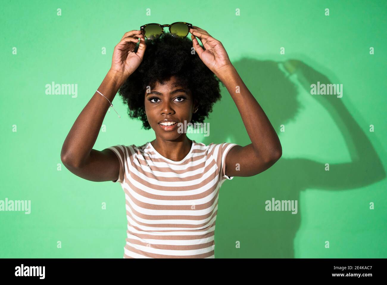 Femme portant des lunettes de soleil sur la tête tout en se tenant contre le vert arrière-plan Banque D'Images