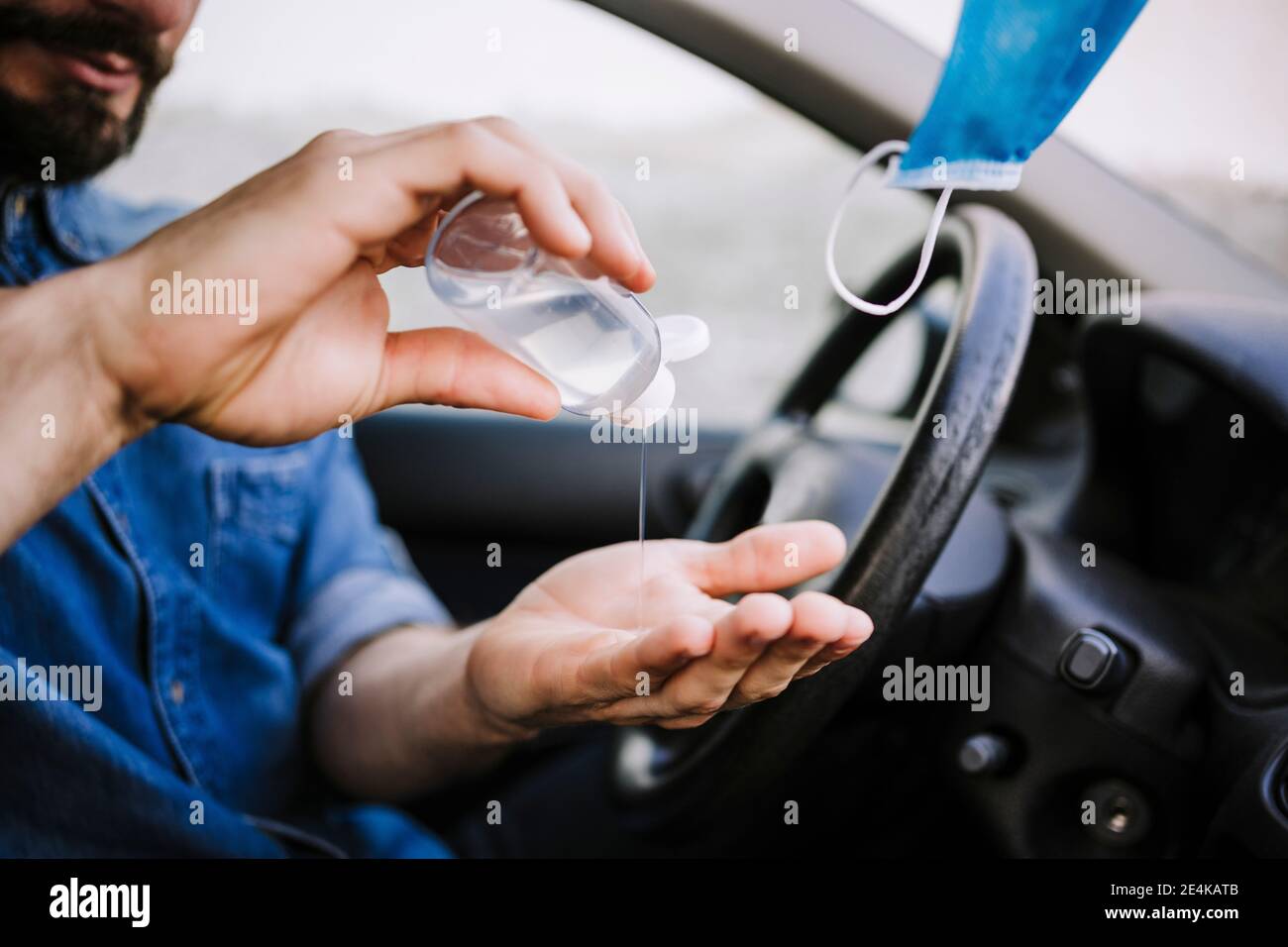 Jeune homme utilisant de l'assainisseur pour les mains en voiture pendant le COVID-19 Banque D'Images