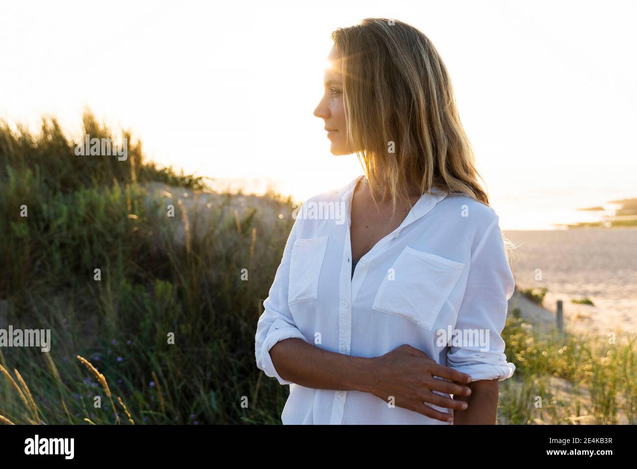Femme adulte de taille moyenne regardant loin en se tenant près d'une dune de sable Banque D'Images