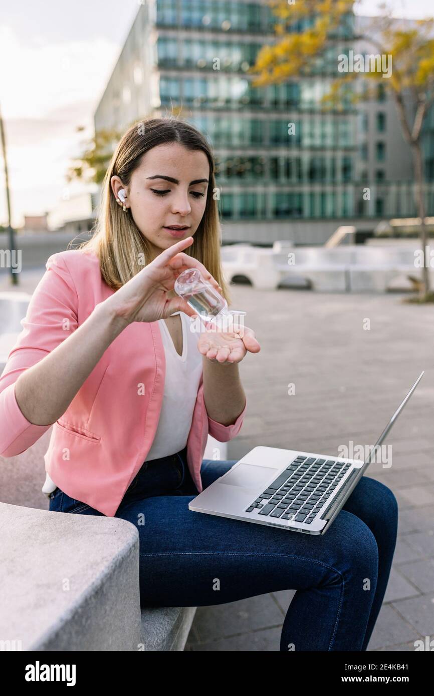 Espagne, Barcelone, jeune femme d'affaires avec ordinateur portable utilisant l'assainisseur pour les mains à l'extérieur Banque D'Images