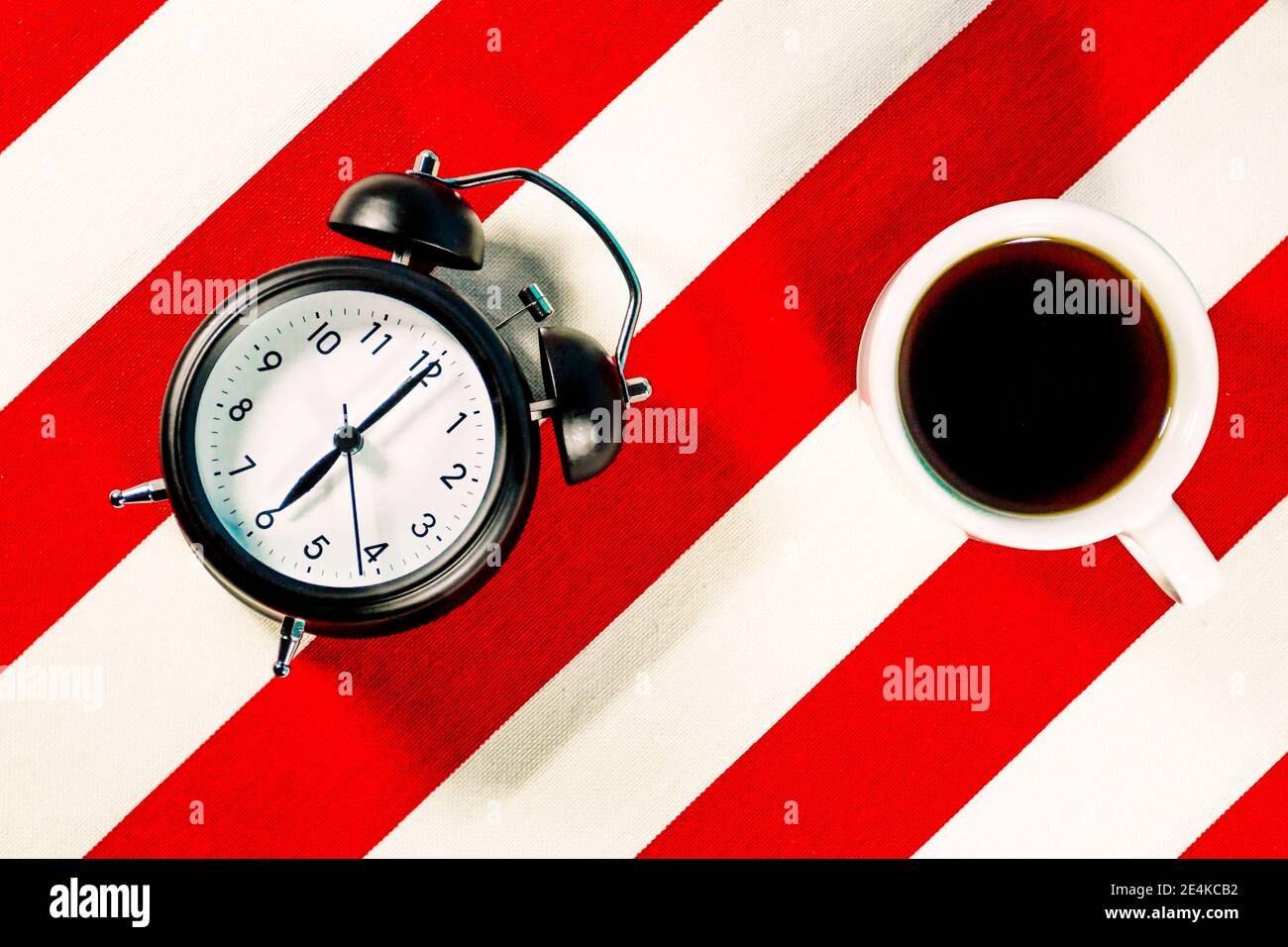 Tasse de café et réveil sur blanc et rouge motif à rayures Banque D'Images