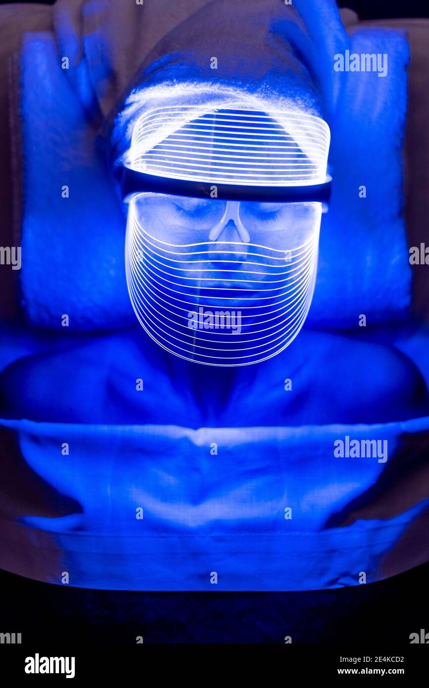 Jeune cliente portant un masque bleu éclairé pendant le traitement de rajeunissement au centre de beauté Banque D'Images