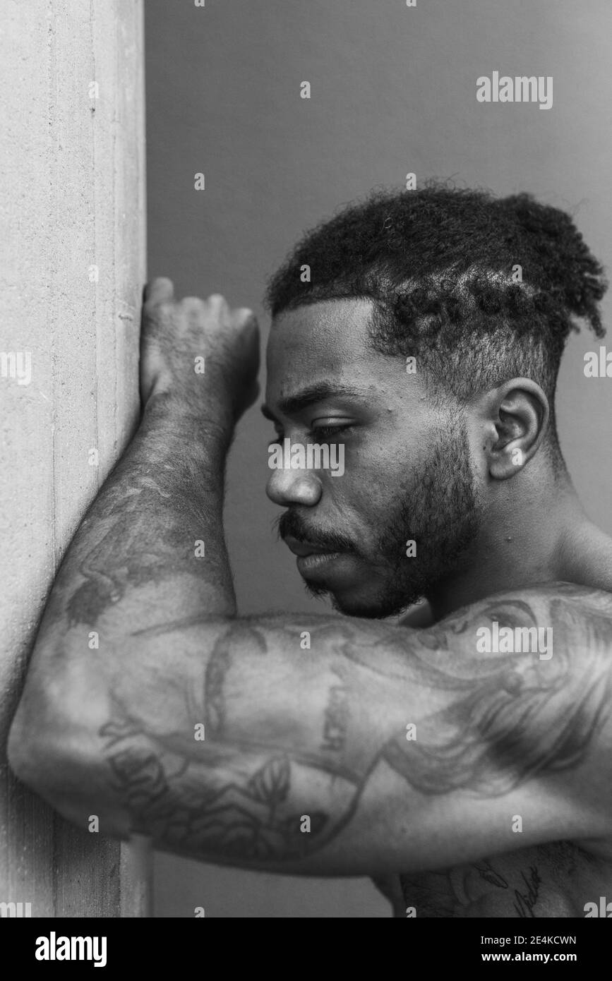 Sportif montrant des biceps avec tatouage tout en s'appuyant sur la colonne Banque D'Images