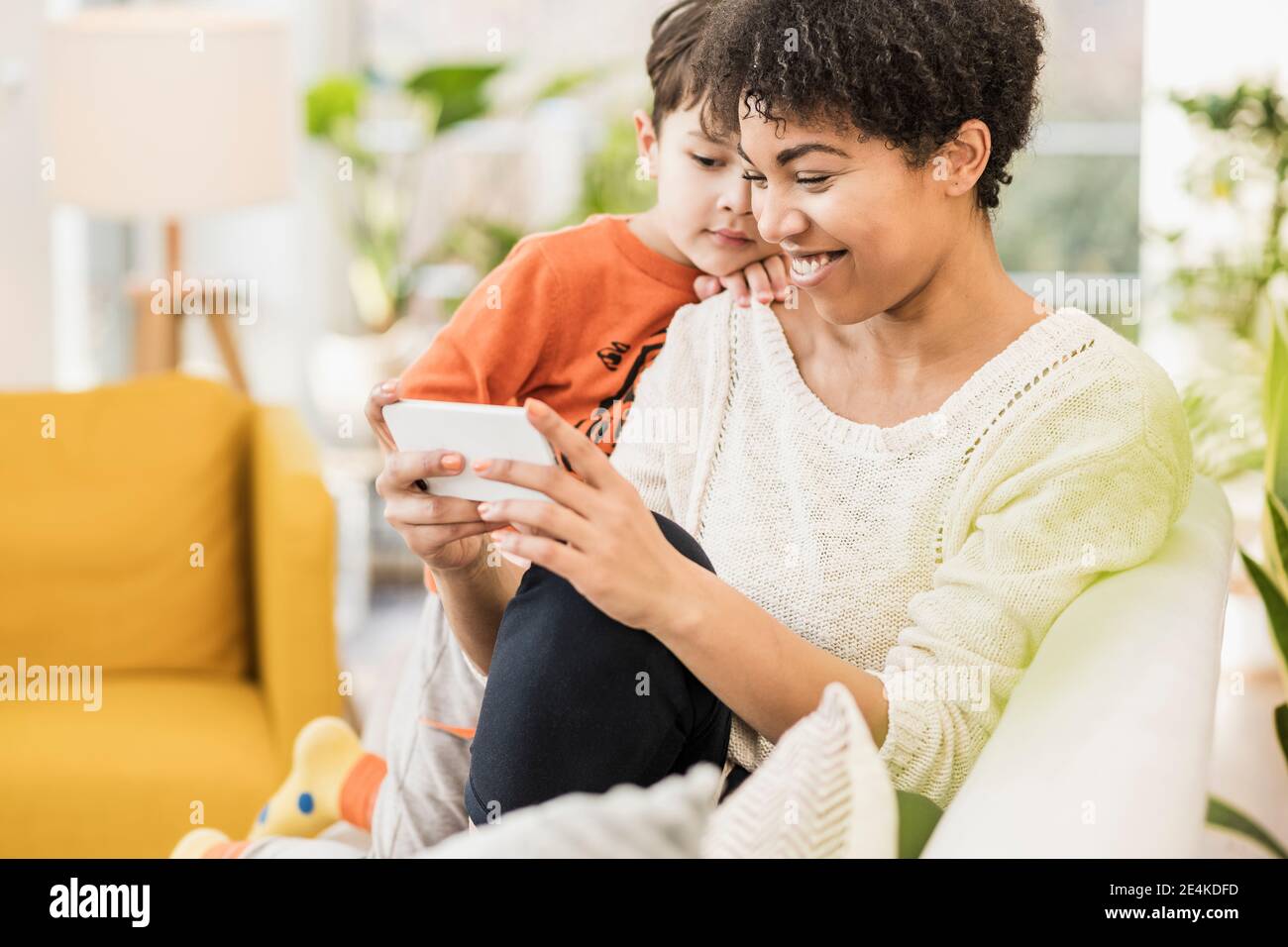 Mère utilisant un téléphone portable tout en étant assise par frère sur le canapé à la maison Banque D'Images