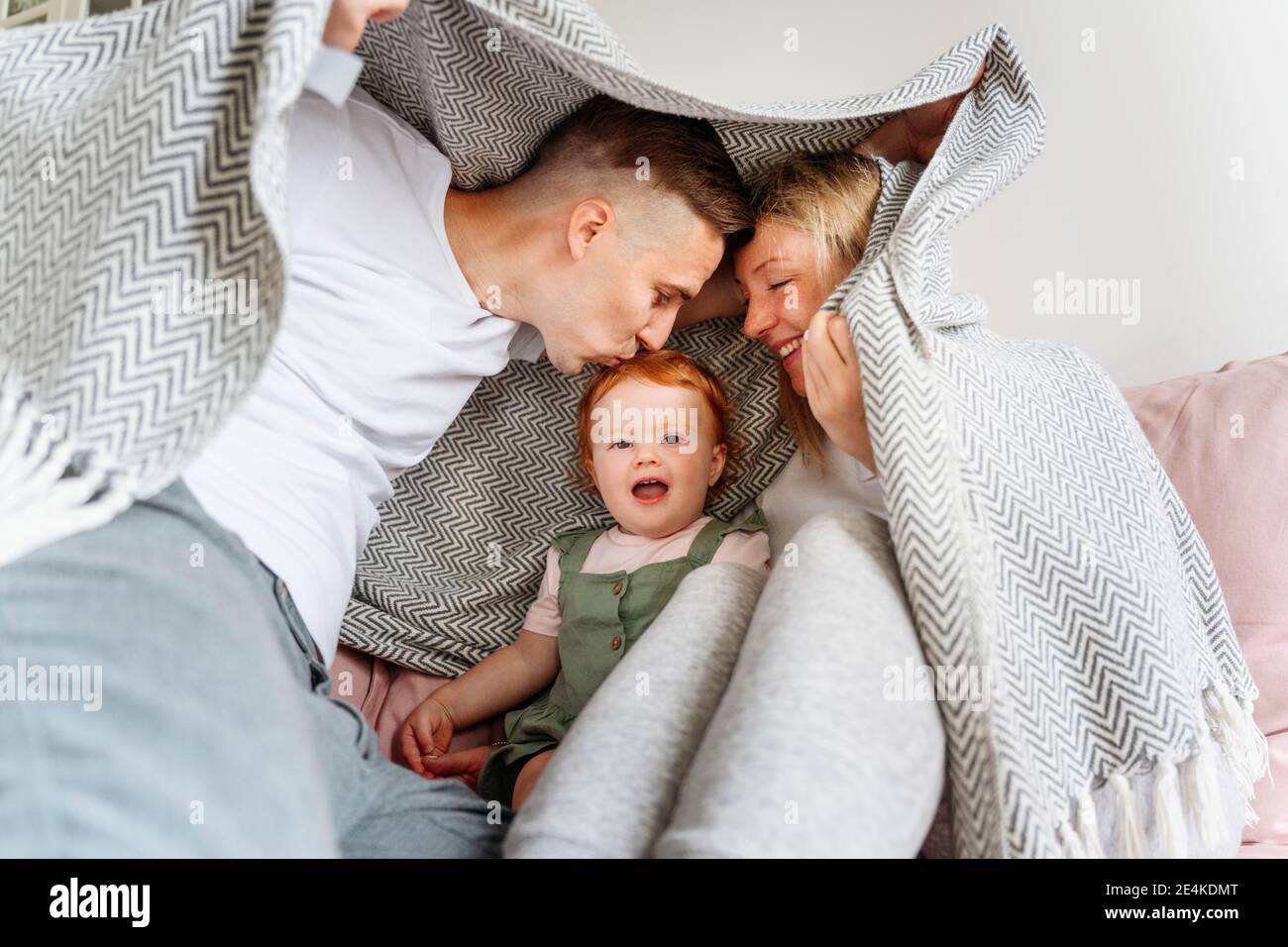 Famille heureuse avec bébé fille se cachant sous une couverture sur le canapé Banque D'Images