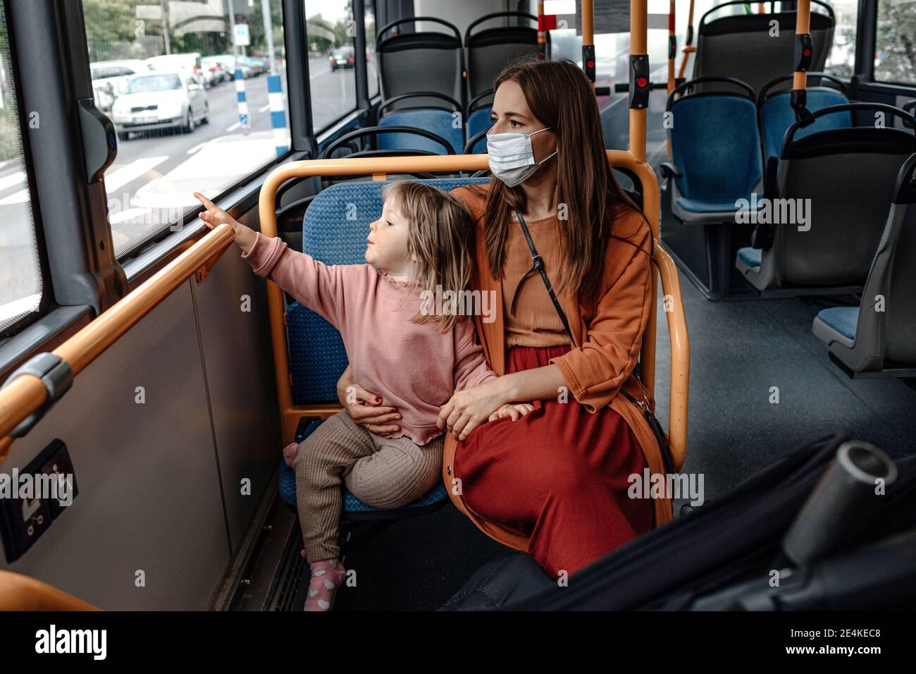 Mère avec une jolie fille pointant vers la fenêtre pendant son voyage Bus pendant COVID-19 Banque D'Images Mère avec une jolie fille pointant vers la fenêtre pendant son voyage Bus pendant COVID-19 Banque D'Images