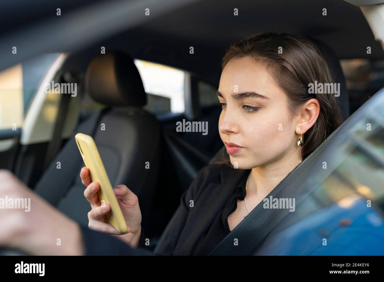Femme d'affaires utilisant un téléphone mobile en étant assise dans la voiture Banque D'Images