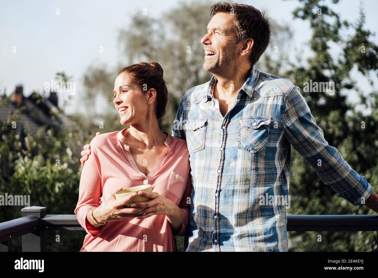 Homme joyeux avec le bras autour de la femme tenant le bol dans balcon par beau temps Banque D'Images