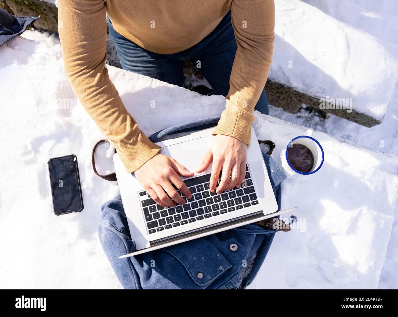 Homme adulte moyen utilisant un ordinateur portable près d'une tasse de café banc recouvert de neige au soleil Banque D'Images