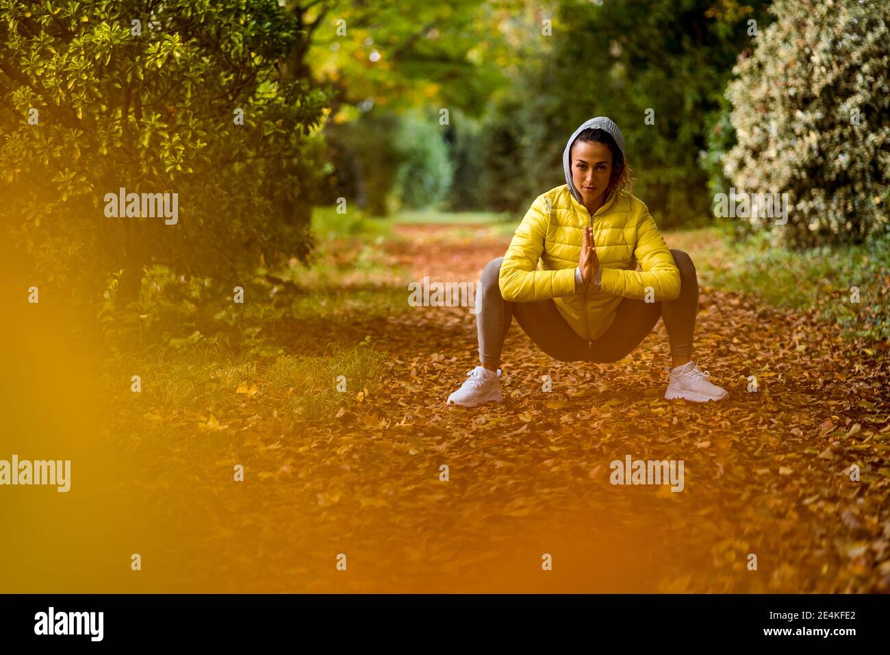 Femme adulte de taille moyenne avec main clasped crouching tout en faisant de l'exercice au parc Banque D'Images