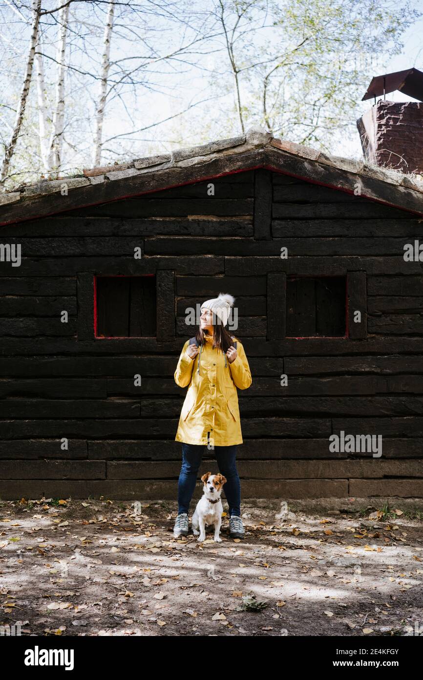 Femme en imperméable jaune debout avec un chien devant chalet en rondins Banque D'Images