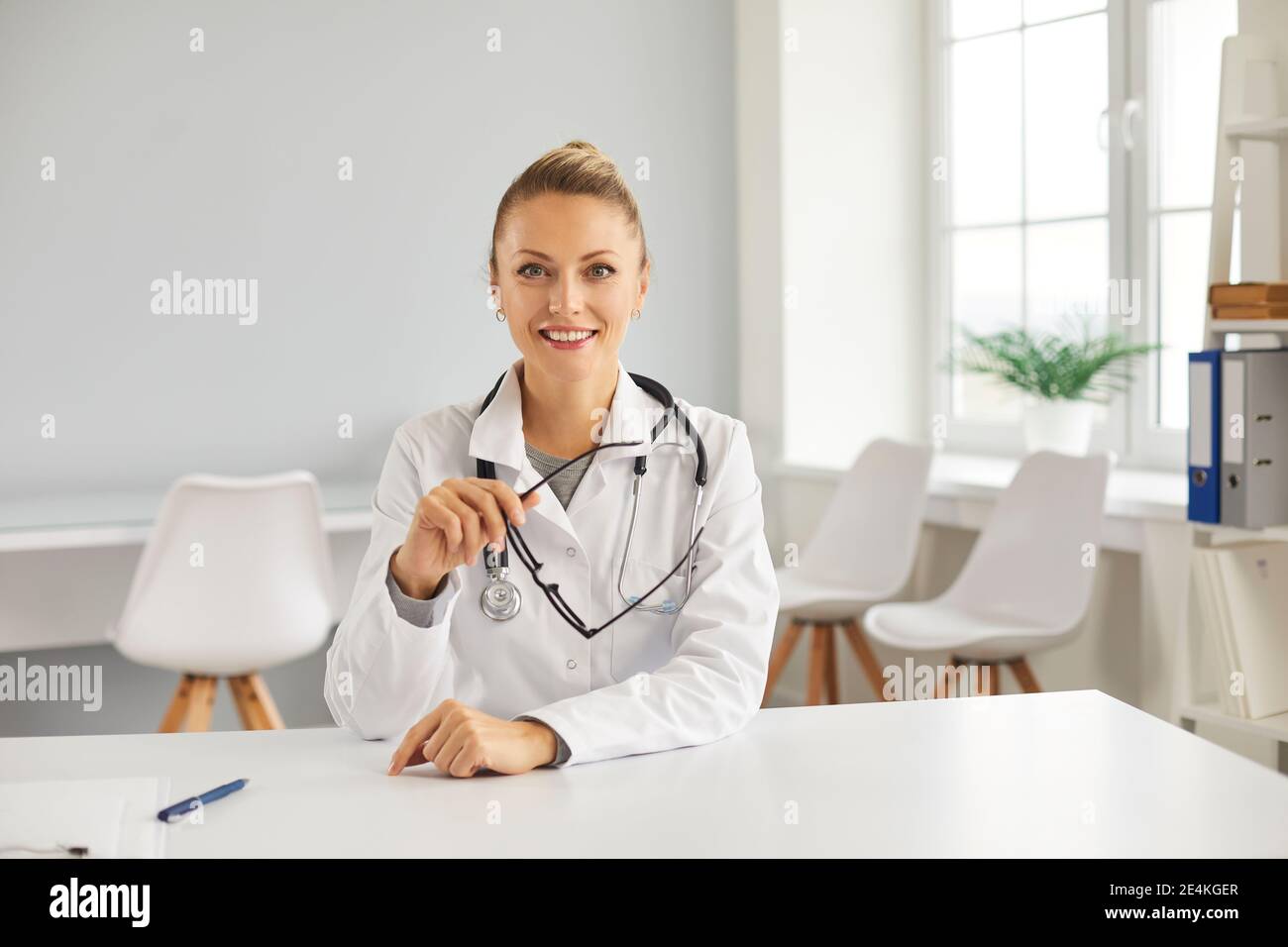 Un jeune médecin heureux assis à table dans son bureau, souriant et regardant l'appareil photo Banque D'Images