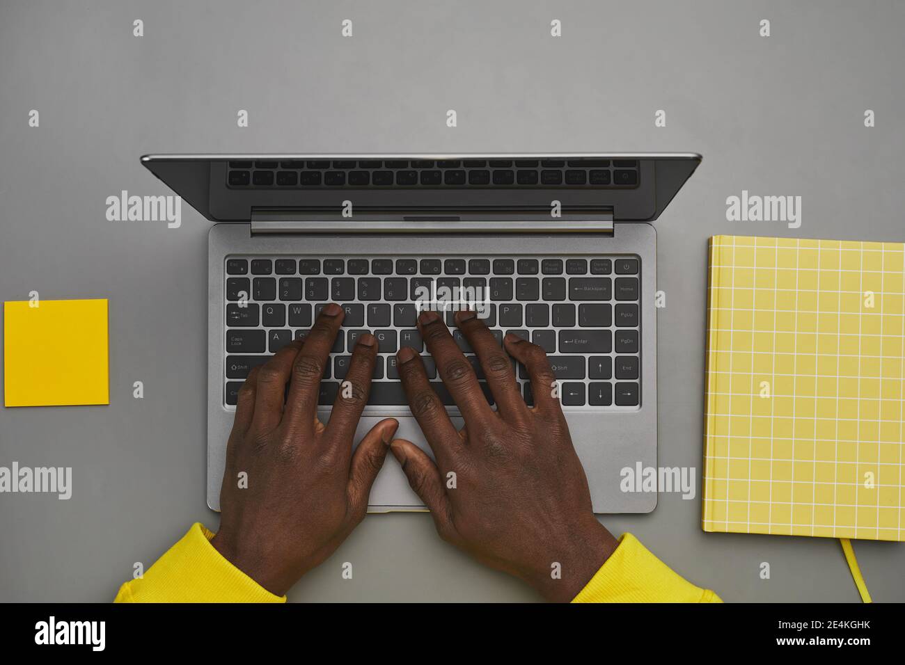 Arrière-plan gris et jaune graphique des mains afro-américaines dactylographiant sur le clavier de l'ordinateur portable tout en travaillant au bureau, vue de dessus vers le bas, espace de copie Banque D'Images