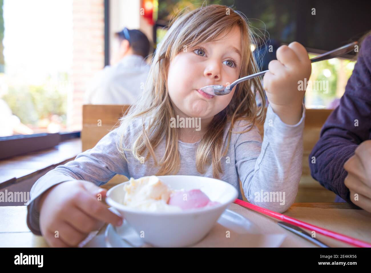 portrait d'un enfant blond de trois ans qui mange de la glace à la fraise et à la vanille avec une cuillère dans un bol blanc, assis à la table du restaurant Banque D'Images