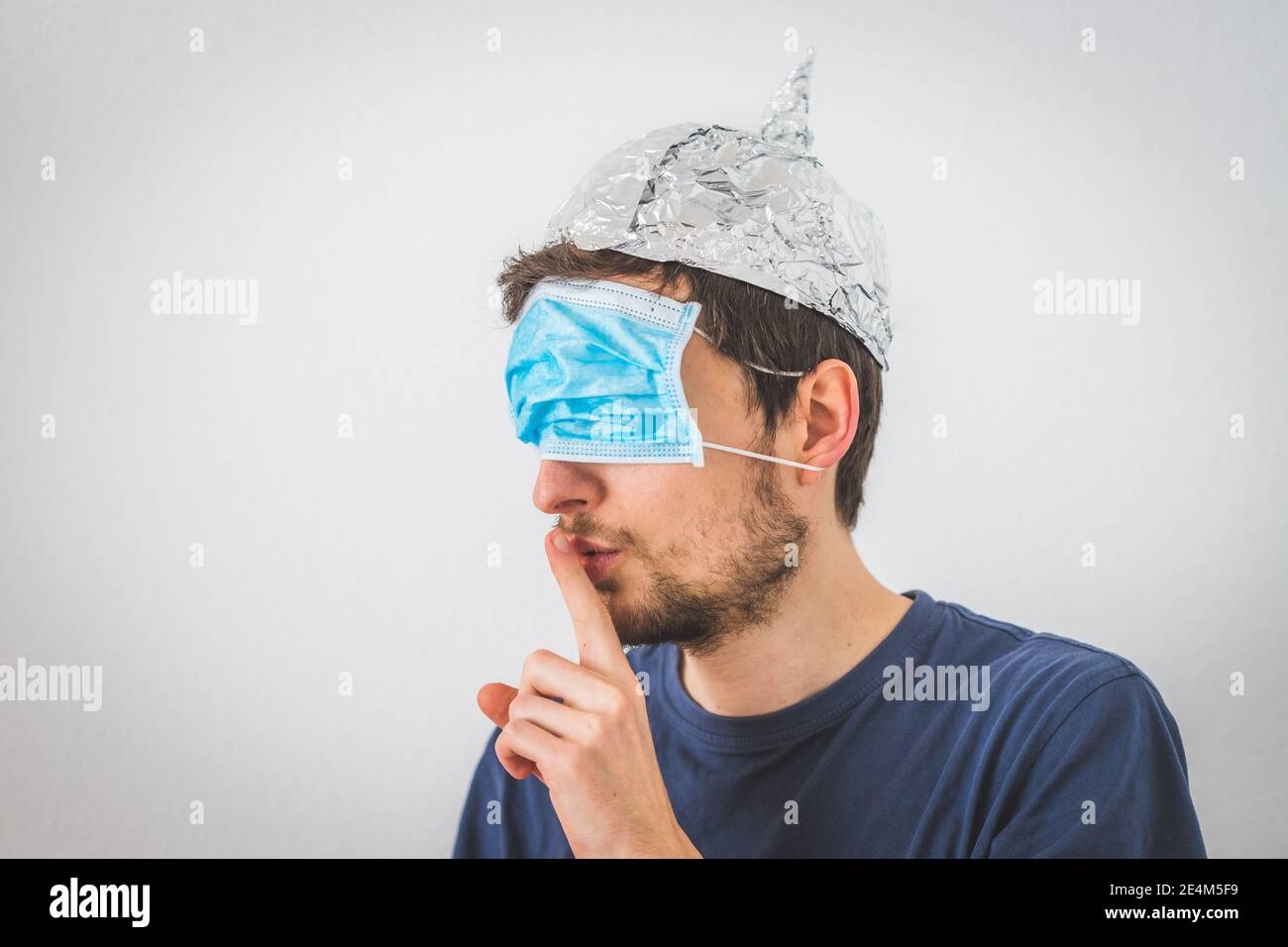 Jeune homme en colère avec masque facial sur les yeux et chapeau en aluminium fait un psst! geste Banque D'Images