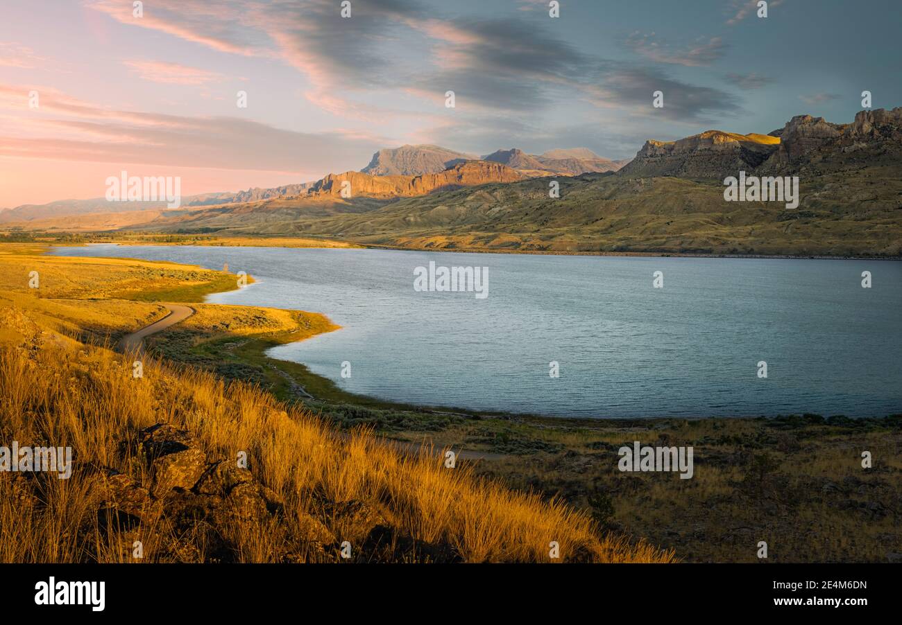 Admirez le long de la rivière Shoshone avec des herbes et des rochers et des contreforts des montagnes Rocheuses à l'horizon sous un ciel coloré au crépuscule près de Cody, Wyoming, États-Unis. Banque D'Images