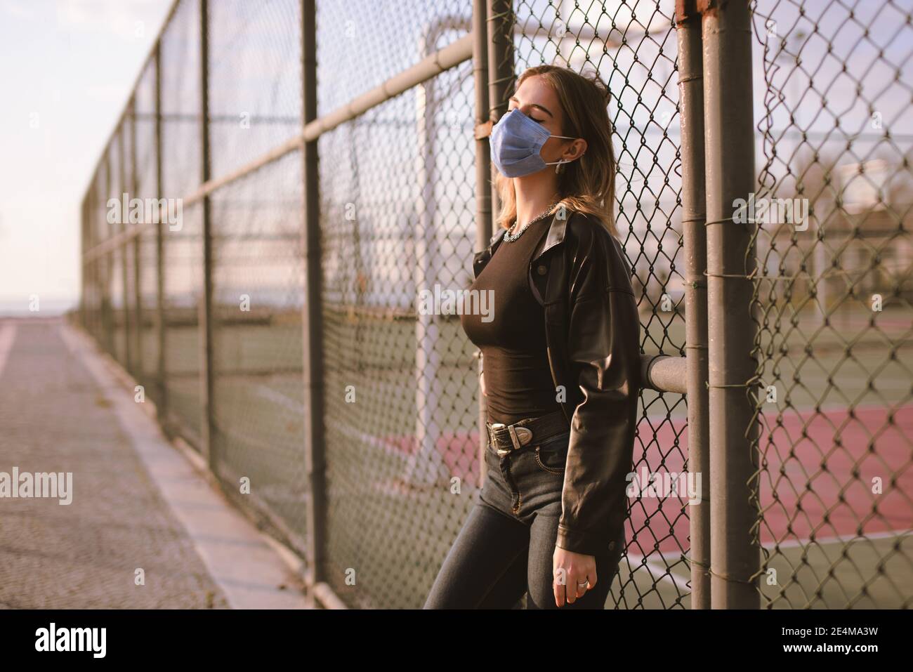Portrait d'une adolescente avec un masque médical dans la rue, et penchée à une clôture. Banque D'Images