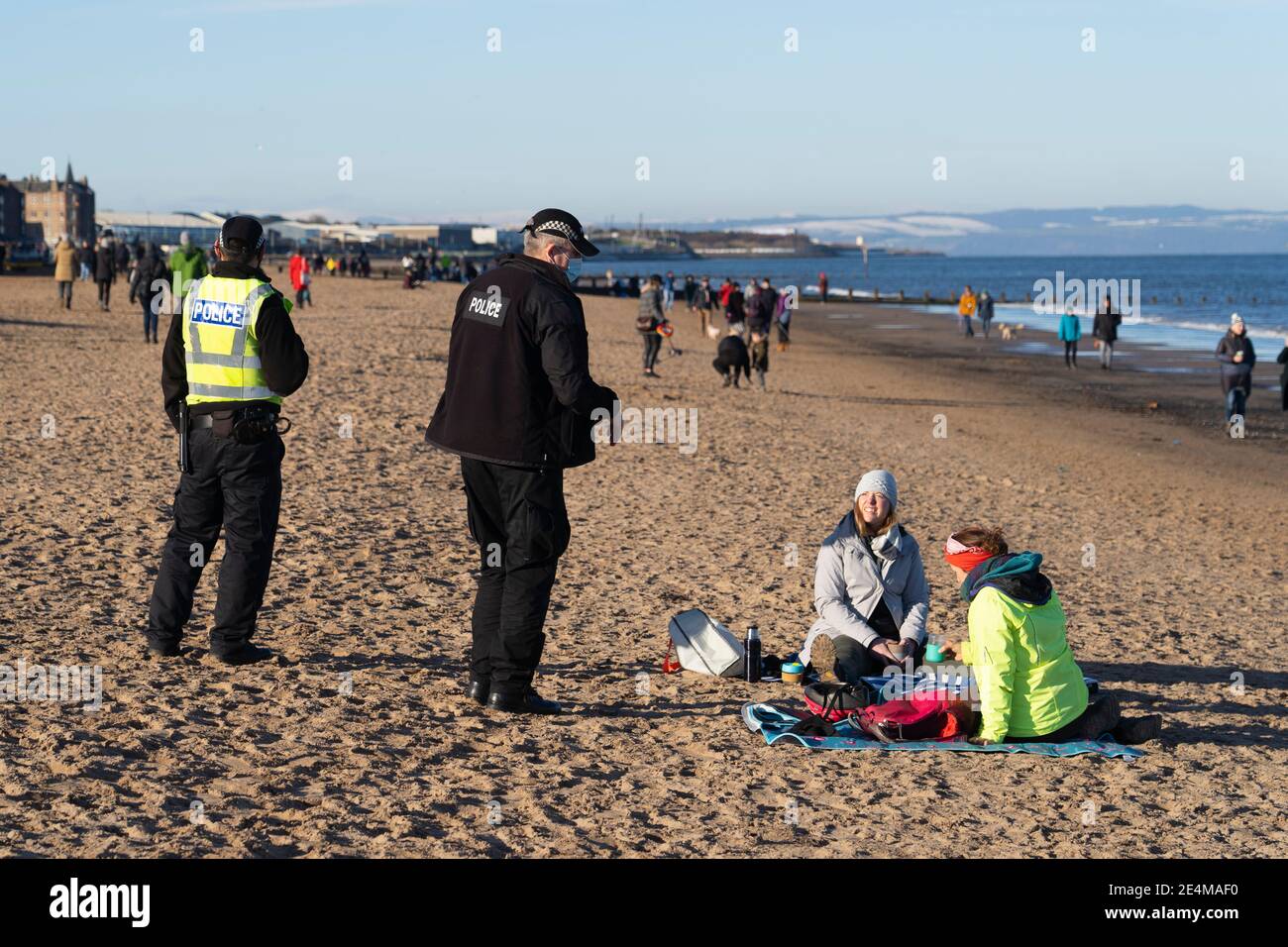 Portobello, Écosse, Royaume-Uni. 24 janvier 2021. Grand nombre de membres du public à Portobello Beach et promenade le dimanche après-midi ensoleillé pendant l'isolement. Alors que la plupart des gens ont observé des groupes sociaux distanciants de personnes se sont formés dans certains des cafés offrant des plats à emporter et des boissons. Les patrouilles de police ont parlé au public assis et en groupes dans les cafés pour leur demander de continuer. Pic; la police demande à deux membres du public de ne pas s'asseoir sur la plage. Iain Masterton/Alay Live News Banque D'Images