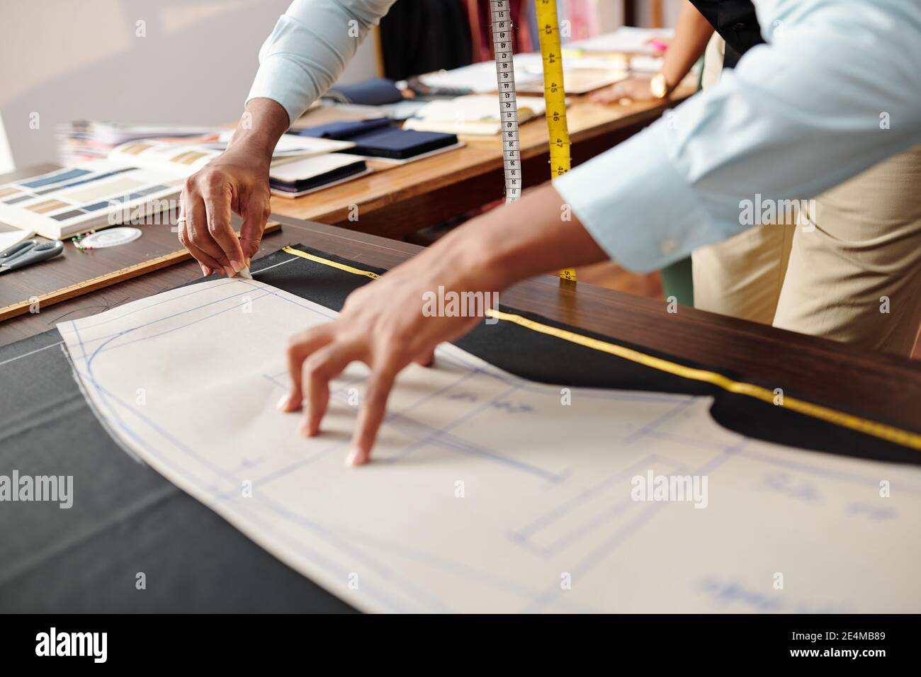 Des mains de tailleur tracer le motif de couture sur le tissu noir quand fabrication de pantalons pour le client Banque D'Images