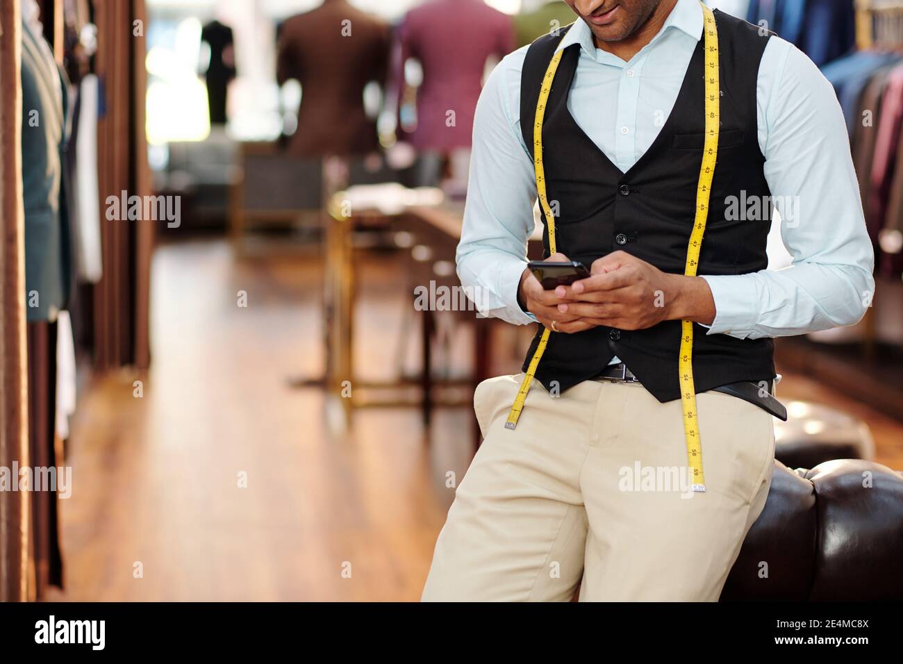 Image rognée d'un jeune tailleur incliné sur la chaise et de contrôle messages texte sur le smartphone pendant la pause Banque D'Images