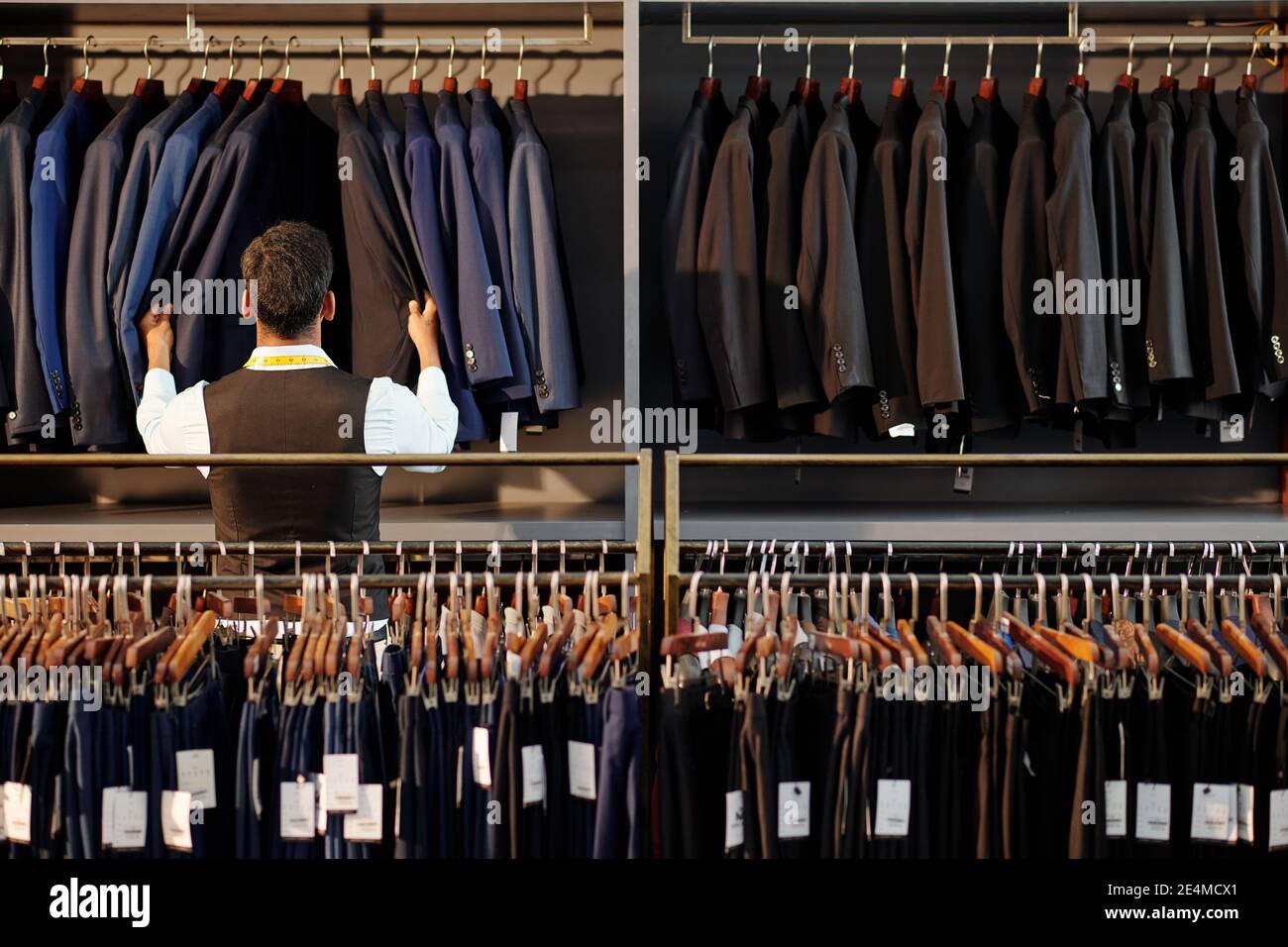 Assistant-boutique vérifiant les vestes sur le cintre dans le magasin de vêtements pour hommes, vue de l'arrière Banque D'Images