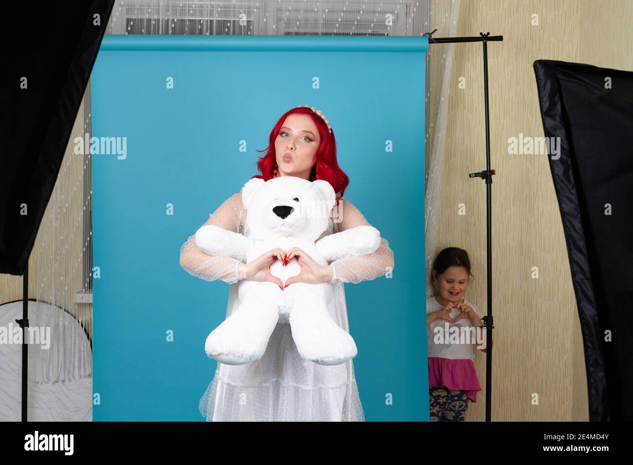 Maison studio de photo, un modèle dans une robe blanche et un ours en peluche pose pour la Saint-Valentin, une fille lance et répète pose Banque D'Images