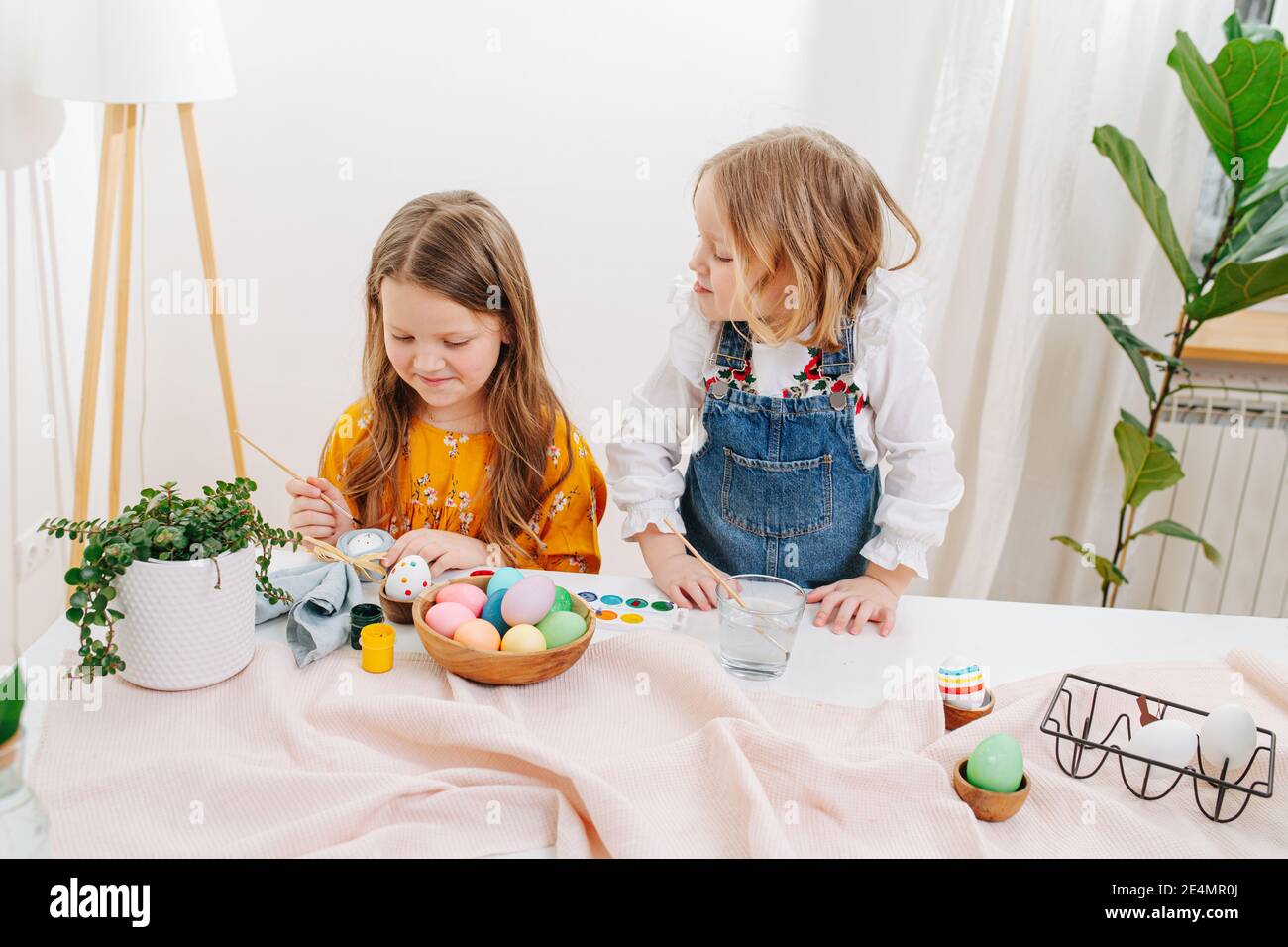Deux petites filles peignent des œufs de pâques derrière une table Banque D'Images