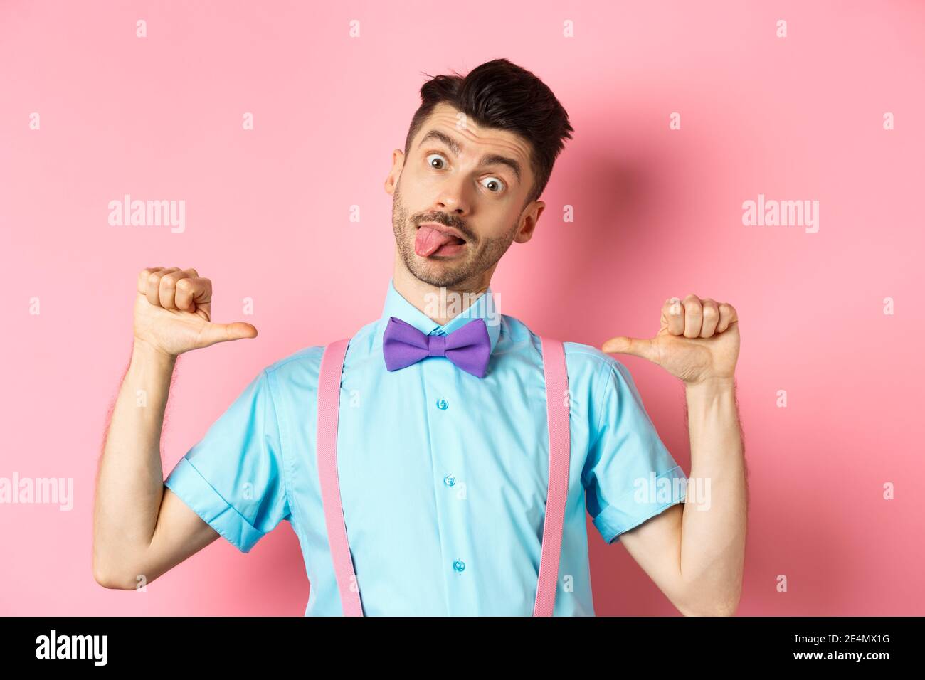 Drôle de type dans les bretelles et noeud papillon montrant la langue,  pointant vers lui-même comme si auto-promotion, debout sur fond rose Photo  Stock - Alamy