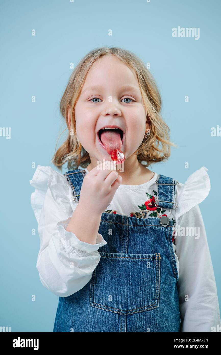 Bonne petite fille blonde aime manger des bonbon de Lollipop sur bleu Banque D'Images
