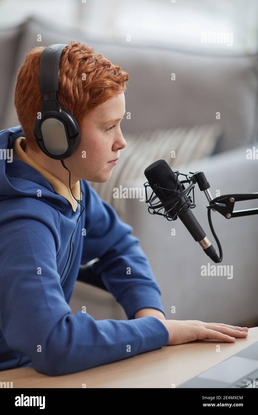 Portrait vertical de l'adolescent à cheveux rouges parlant permet d'utiliser un microphone et un casque pendant l'enregistrement d'un podcast ou en ligne flux Banque D'Images