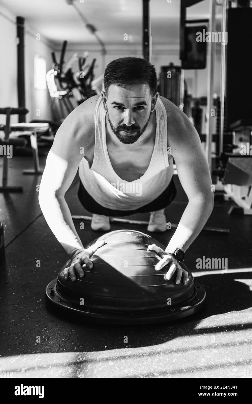 Homme s'exerçant sur le bosu ball dans la salle de gym en noir et blanc. Concept santé et bien-être. Sport. Banque D'Images