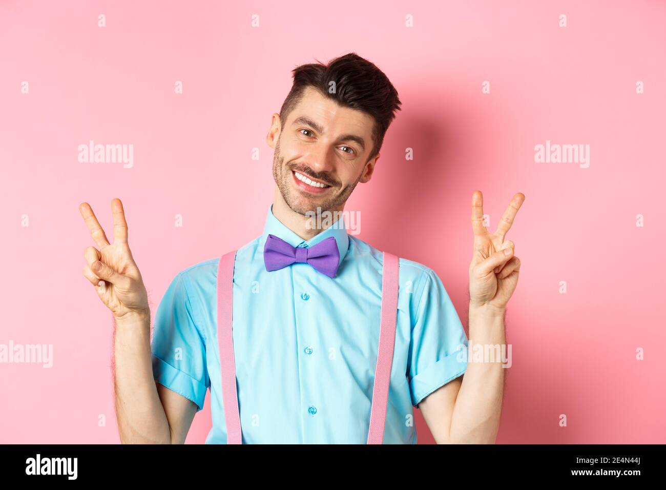 Romantique gars en noeud papillon et bretelles montrant des signes de paix  et souriant à la caméra, portant des vêtements pour la date, debout sur  fond rose Photo Stock - Alamy