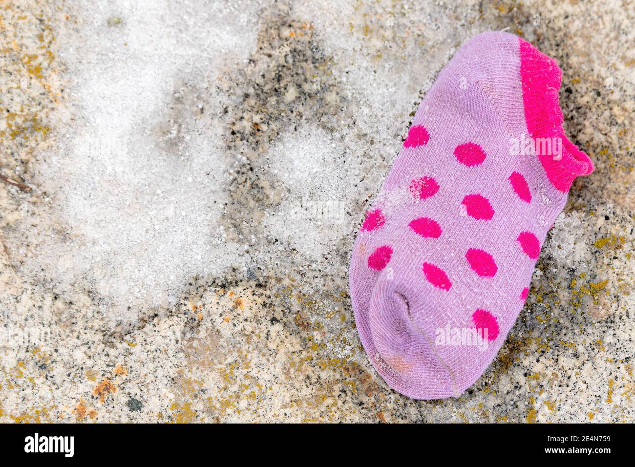 Une seule chaussette perdue pour enfant posée sur le sol. La chaussette est petite et pourpre, avec une petite quantité de neige à côté. Vue directement vers le bas par le dessus. Banque D'Images