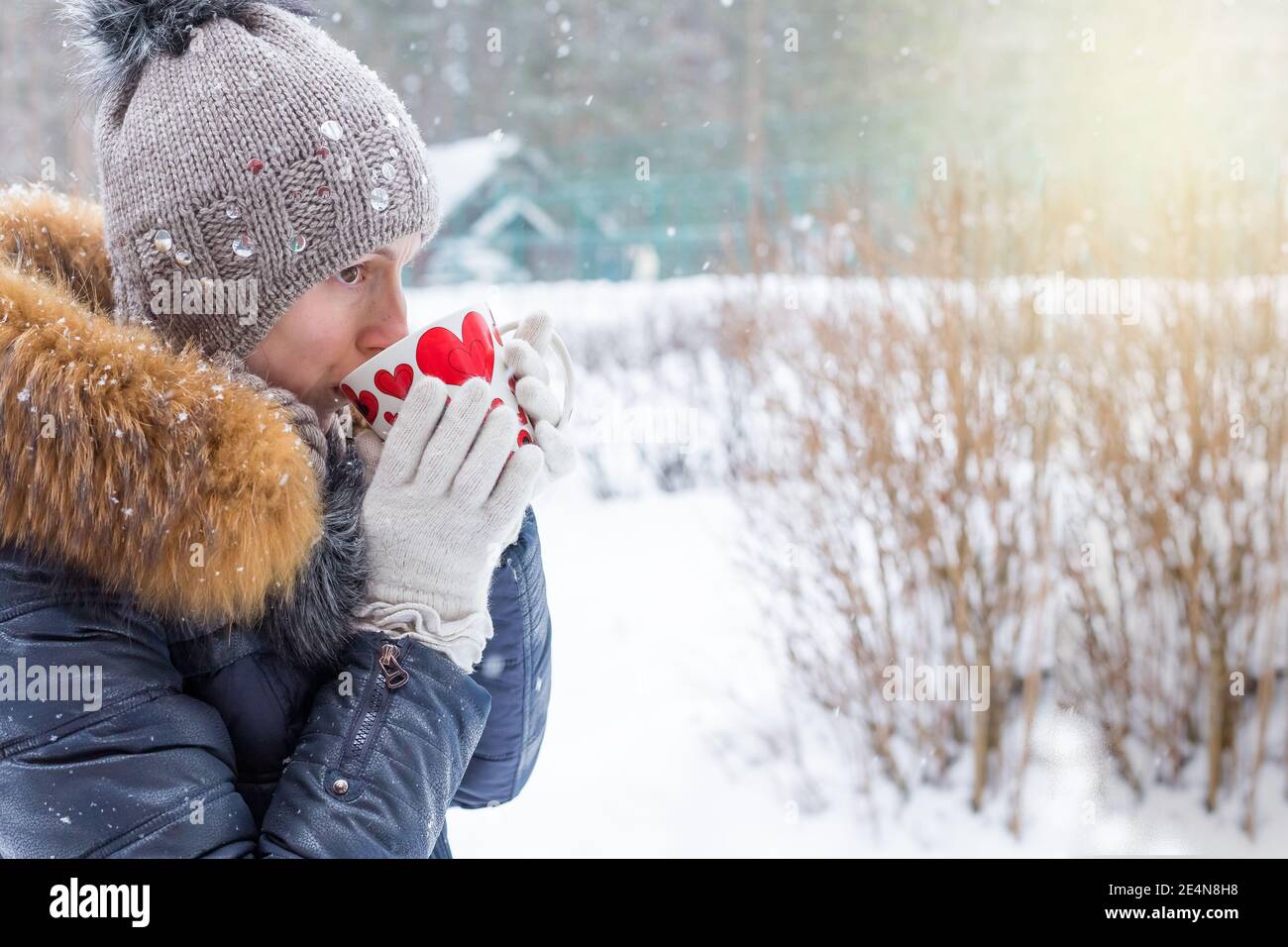 femme d'âge moyen tenant une tasse de boisson chaude et souriant à l'arrière-plan d'une rue d'hiver. photographie en plein air. Banque D'Images